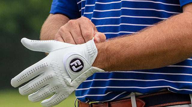 Zbliżenie na dłonie mężczyzny, który zakłada białą skórzaną rękawiczkę golfową z wyraźnym logo FootJoy "FJ"