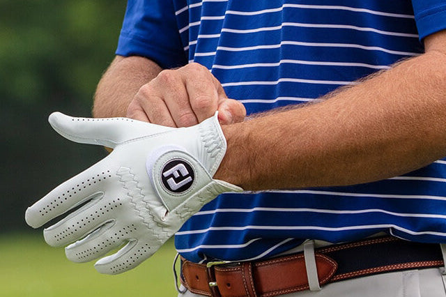 Zbliżenie na dłonie mężczyzny, który zakłada białą skórzaną rękawiczkę golfową z wyraźnym logo FootJoy "FJ"